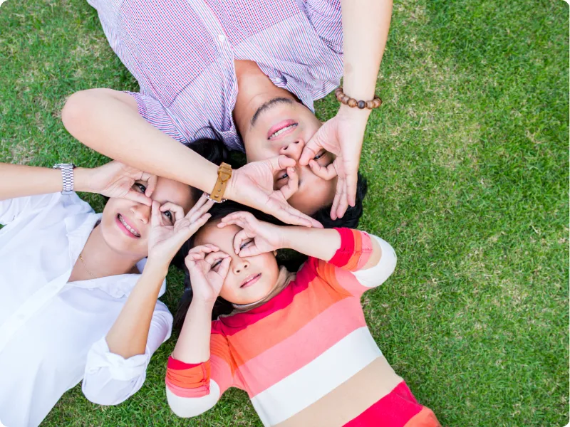 family laying on the grass making glasses with their hands