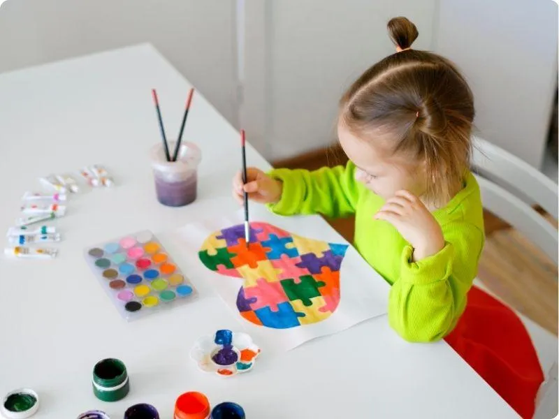 girl painting a heart made of puzzle pieces in different bright colours