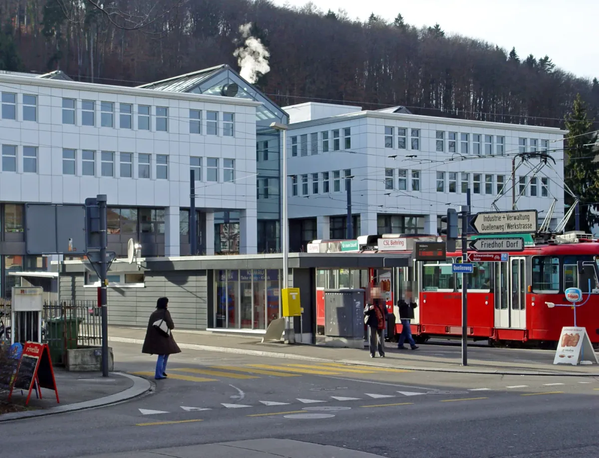 Immeuble de bureaux blanc à plusieurs étages, derrière un arrêt de tram où stationne un tram rouge