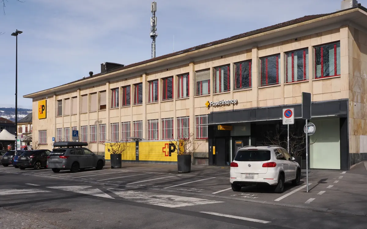 Bâtiment de La Poste à Yverdon-les-Bains avec l'enseigne PostFinance au-dessus de l'entrée, voitures garées devant