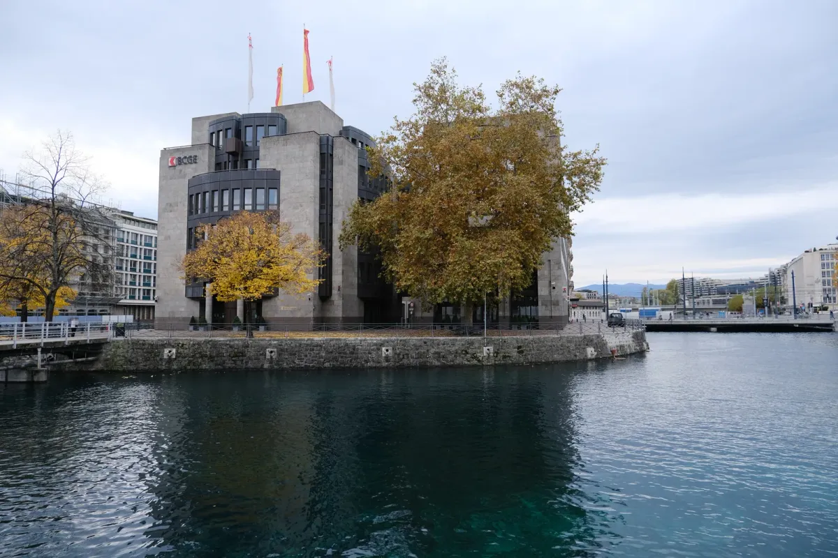 Immeuble de la Banque cantonale de Genève sur l'île du Rhône, entouré d'arbres aux feuilles jaunes, au bord de l'eau