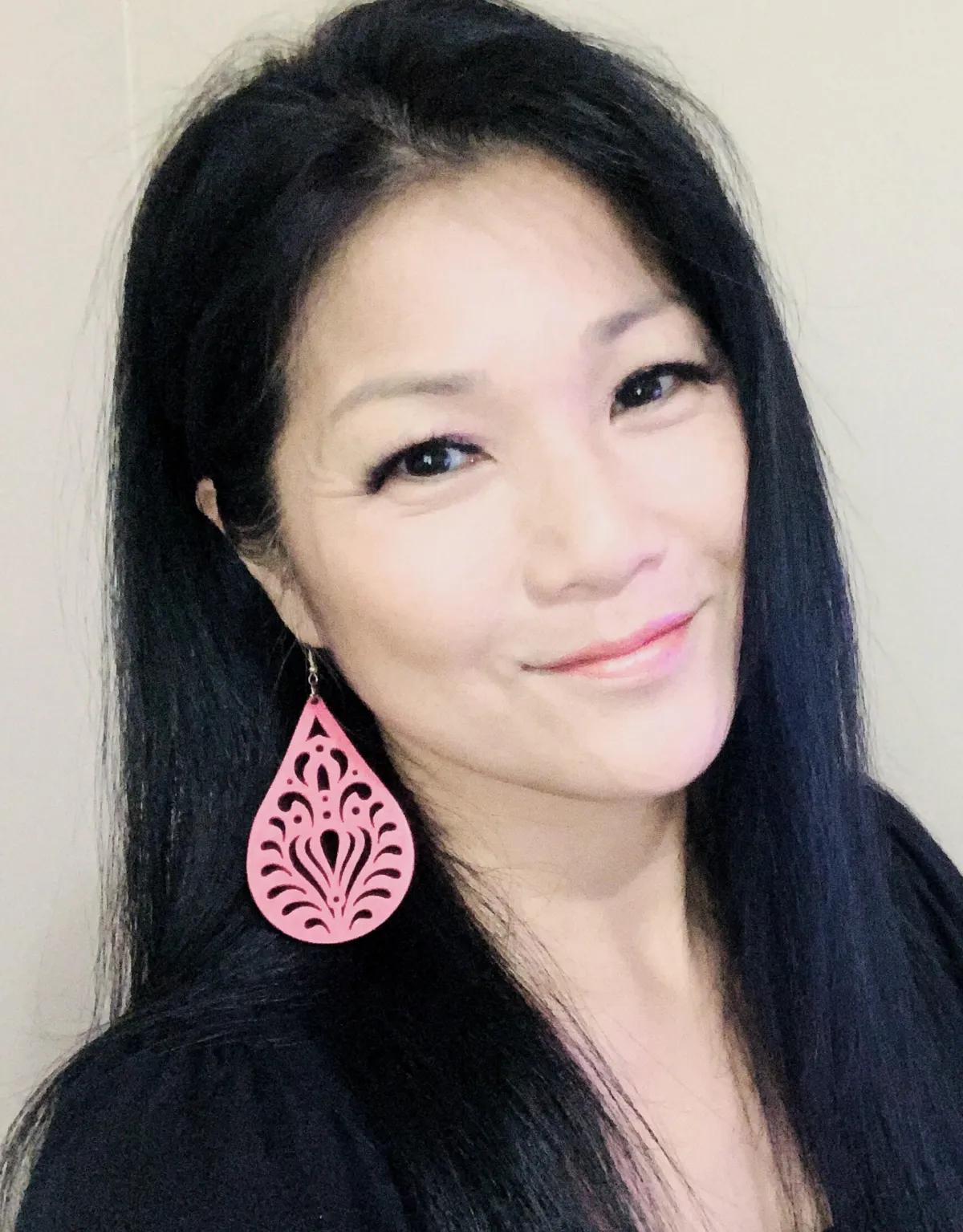 A woman with long, sleek black hair wears a large pink earring featuring an intricate design