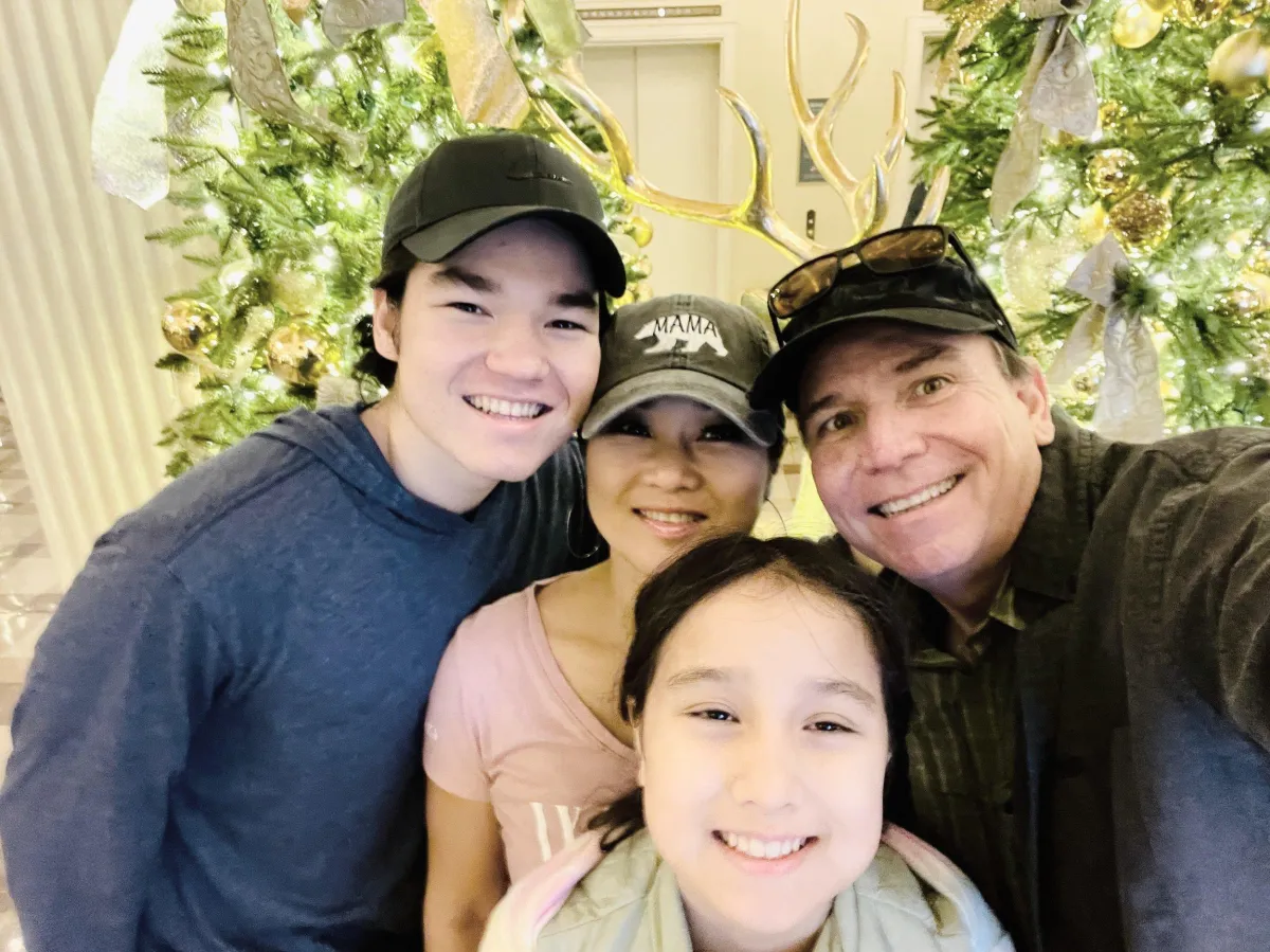 A festive group selfie in front of decorated Christmas trees with golden ornaments and ribbons