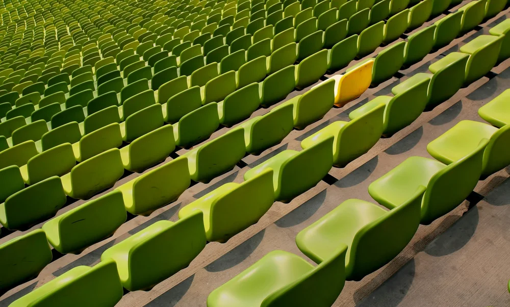 rows of empty green stadium seats with a single yellow seat among them