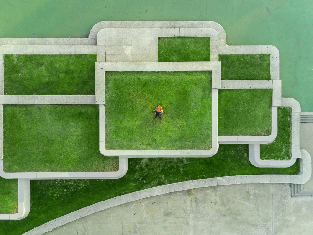 The image shows a person lying in the middle of a structured green space, blending relaxation with an orderly environment.