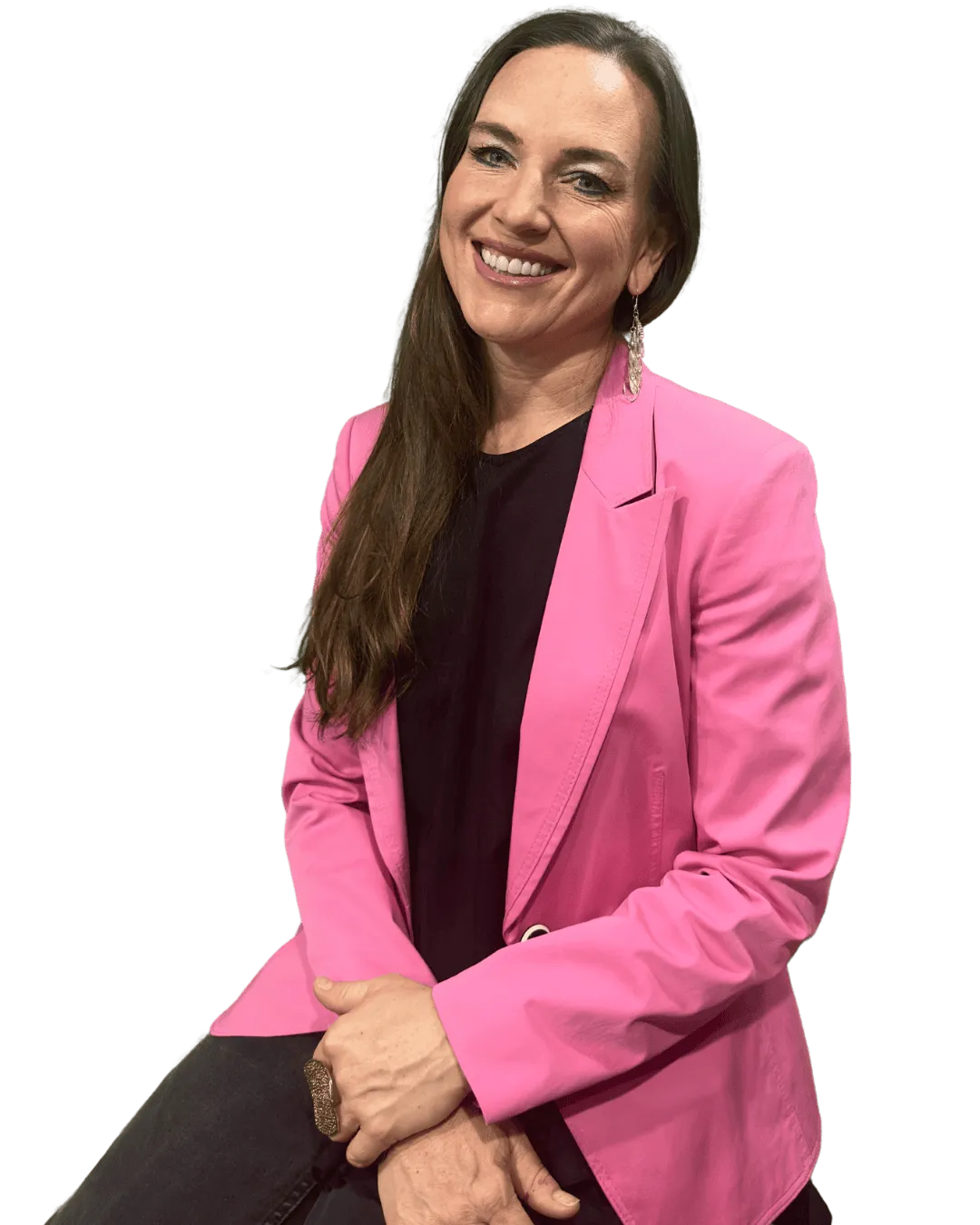 Woman smiling warmly while seated, wearing a bright pink blazer, black top, and dangling earrings, with long brown hair.