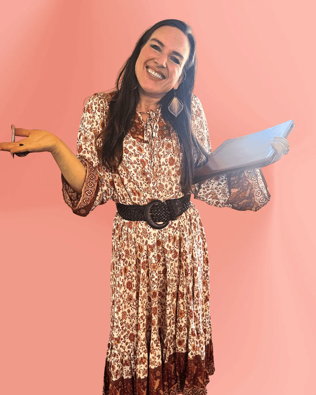 Smiling woman in a patterned bohemian dress holding a folder and pen against a pink background