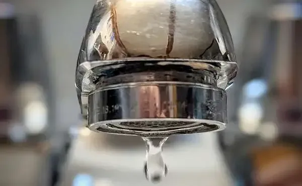 Close-up of chrome kitchen faucet with slow, uneven water drip due to low pipe pressure.