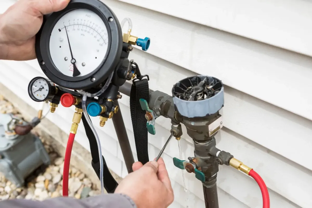 Certified plumber testing backflow preventer with attached pressure gauge and colored hoses.