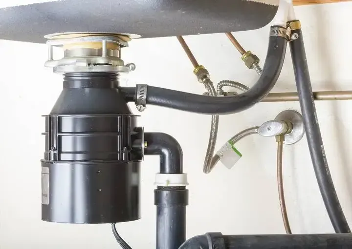 Close-up of a builder-grade garbage disposal prone to clogs, with exposed drain hoses.