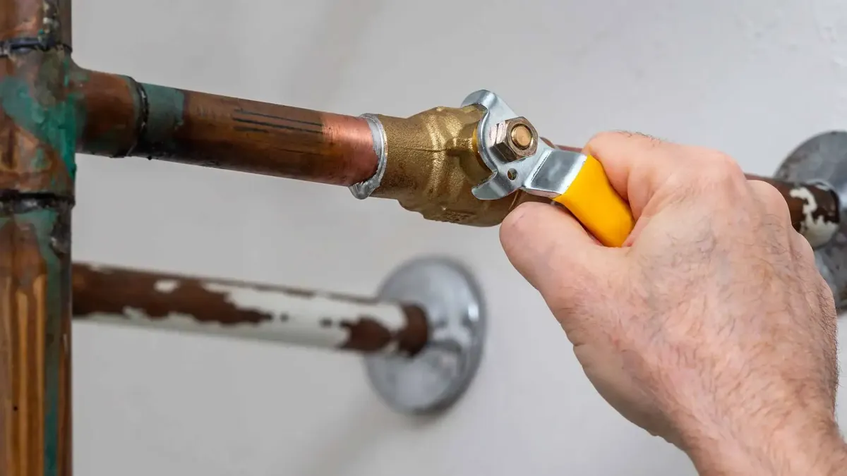 Close-up of plumber manually turning a stuck brass valve on copper piping.