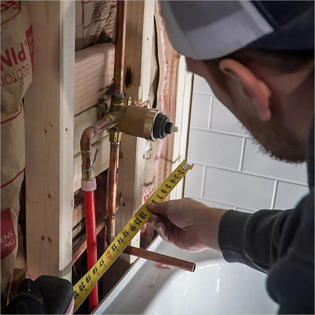 Installer measuring vertical placement of a valve box inside a bathroom wall during remodel.