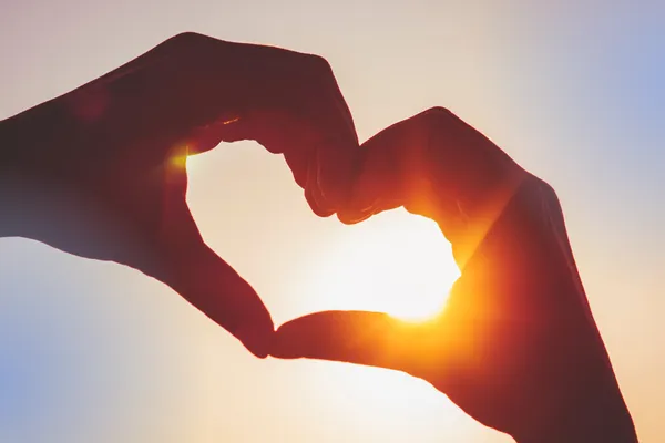 Hands forming a heart shape against a sunset.