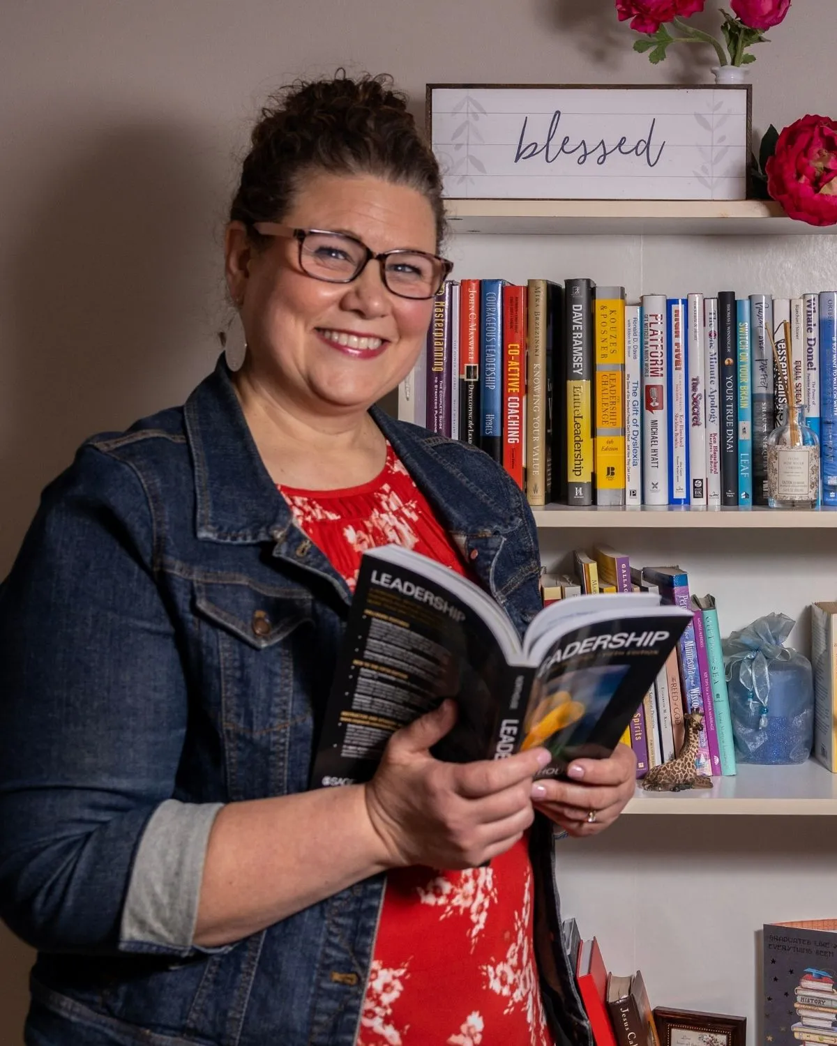 Amy Cummings smiling and holding a leadership book in front of a bookshelf