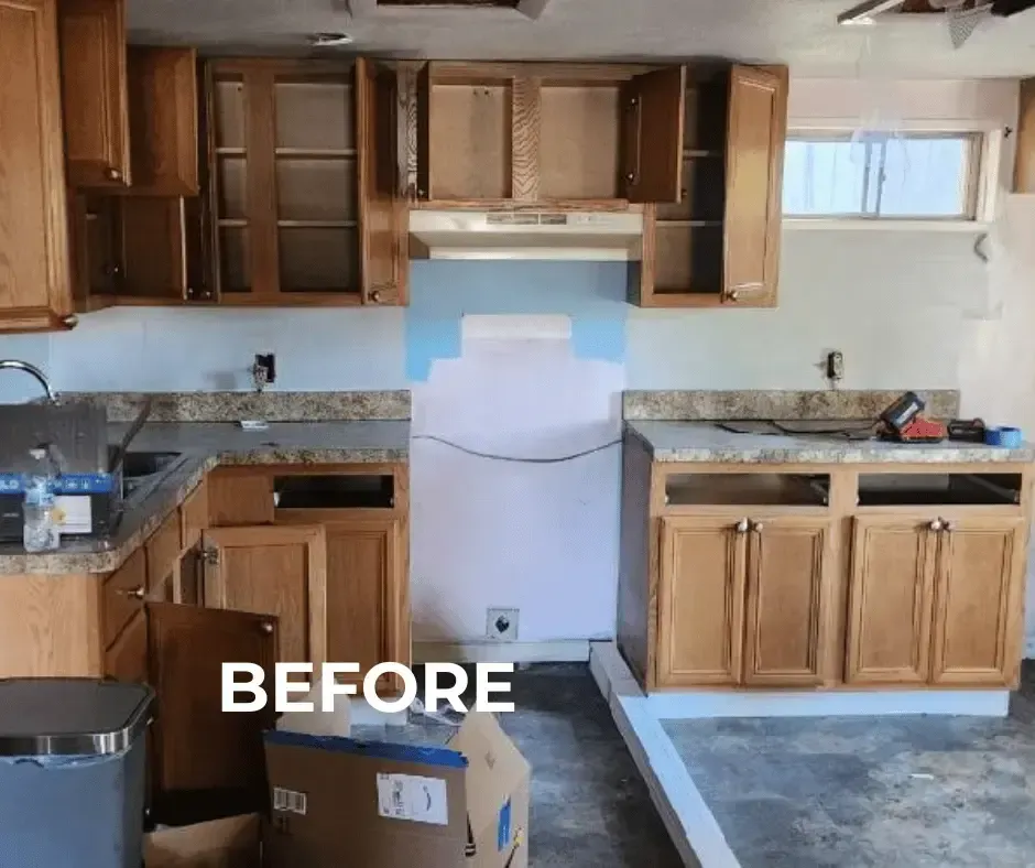 Connecticut basement gut renovation in progress, featuring construction demolition debris in an overflowing grey trash bin, a hanging temporary light fixture, and an unfinished kitchen with partial old cabinets.
