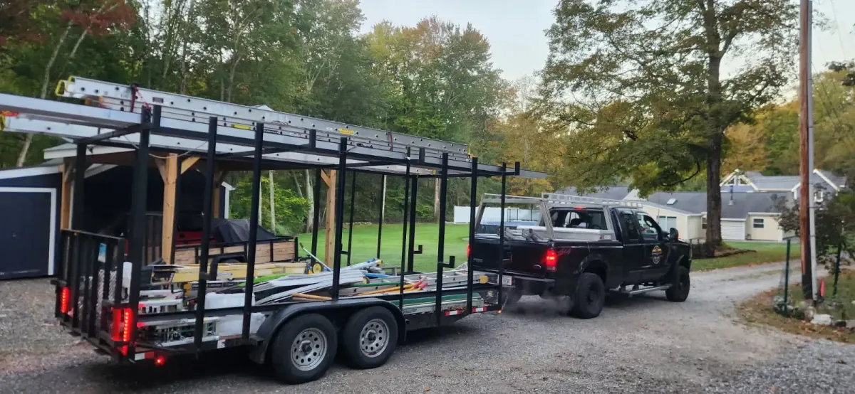 KMAX Renovations commercial contractor pickup truck towing a heavy-duty utility trailer loaded with extension ladders and building equipment to a residential job site in Connecticut.