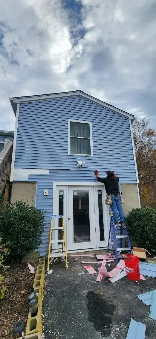 Local Connecticut siding contractor on a ladder installing blue vinyl exterior siding panels around a new front entryway door during a home renovation.