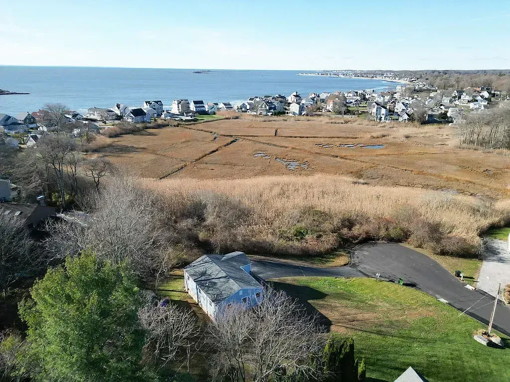 Aerial drone view of a coastal Connecticut shoreline home surrounded by salt marshes and the ocean, representing the local CT residential renovation service area.