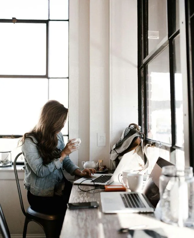 Woman sitting at her kitchen bar with a cup of coffee and laptop, illustrating personalized business support and remote work flexibility.