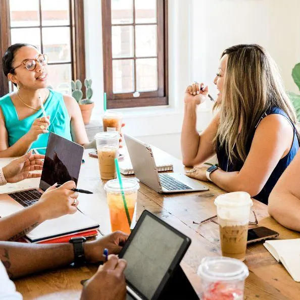 Group of women around a conference table with laptops, having a meeting, symbolizing team support and accountability.