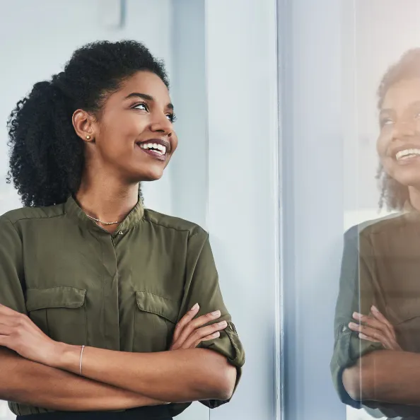 Woman smiling and looking out a window, her reflection visible, symbolizing growth and leadership as a CEO.