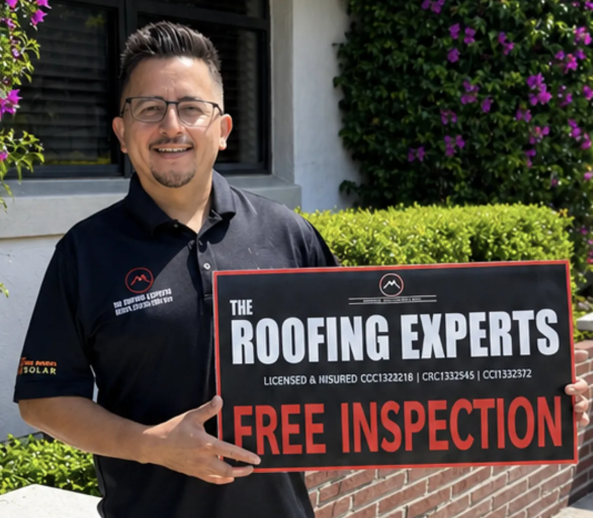 Project Manager from Roofing Experts USA smiling outdoors, wearing sunglasses and a branded polo shirt, with a grassy area and water body in the background.
