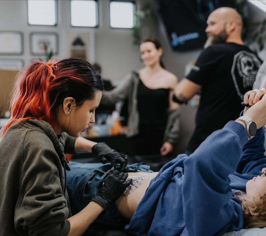 Artist Mia tattooing traditional tattoo inside tattoo shop red arbor