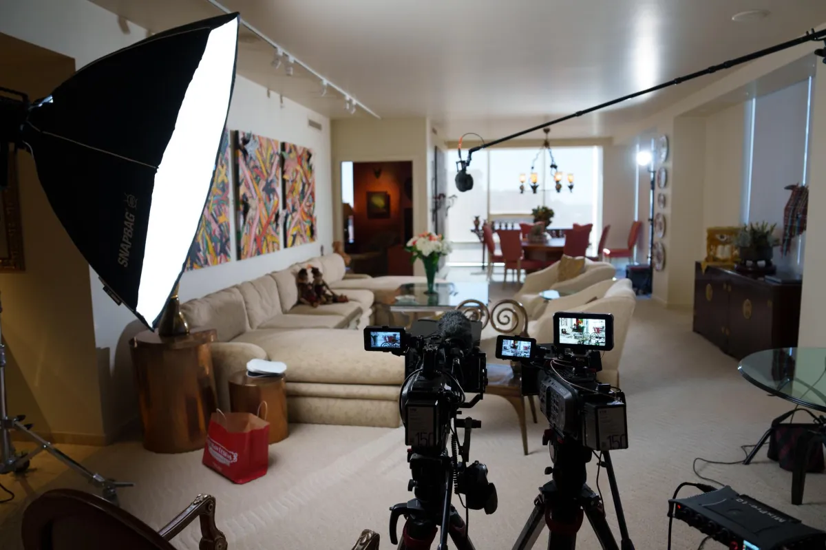 Wide still of an empty indie film classroom with warm tungsten lighting, wooden worktables, and camera kits neatly arranged.