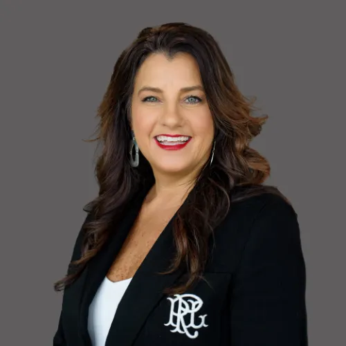 A smiling Asian woman in her late 30s with long black hair, wearing a silk blouse and delicate gold necklace, standing beside a bookshelf filled with design books. The lighting is warm and inviting.