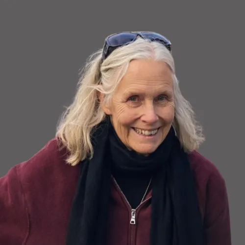 A charismatic man in his 30s with dark skin and a close-cropped beard, wearing a crisp white shirt and gold cufflinks, seated in a velvet armchair. The setting is a high-rise office with panoramic city views.