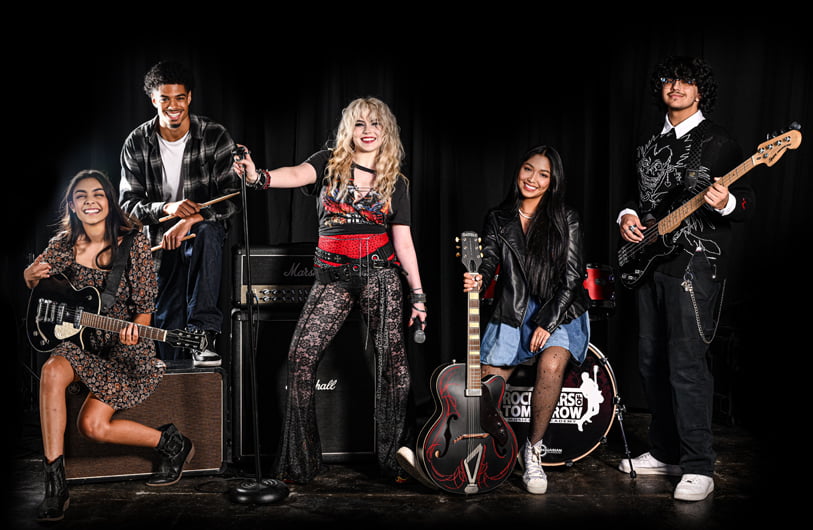 Group of teens playing guitar, bass, drums and singing together during a Rockstars of Tomorrow band performance program.