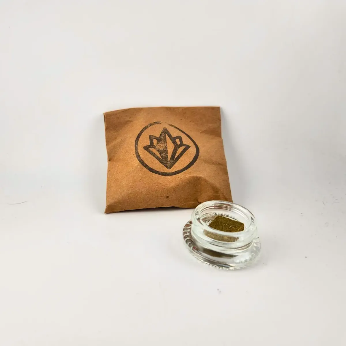 Small jar of Northern Craft Cannabis concentrate with brown paper pouch packaging featuring a black leaf logo in the background