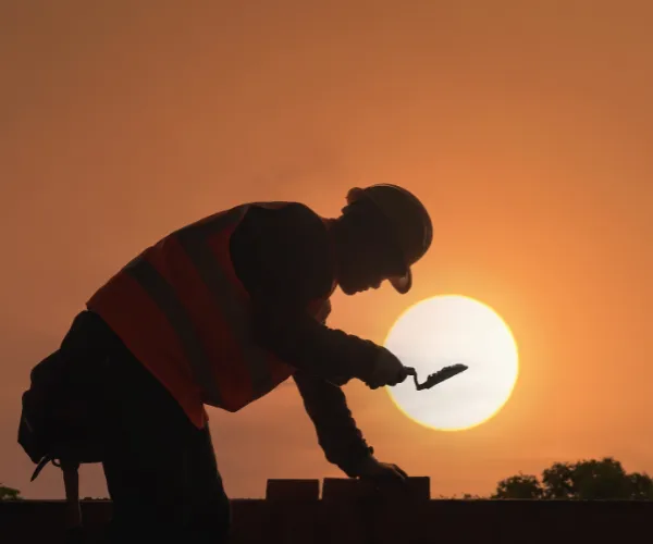 Worker at a Faisalabad construction site carrying bricks and materials for a new housing estate.