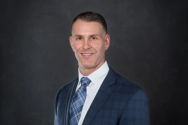 Professional headshot of Jason Moody, CPCU®, Vice President at Centurion Insurance Services, wearing a blue plaid suit, white shirt, and patterned tie, posed against a dark background.
