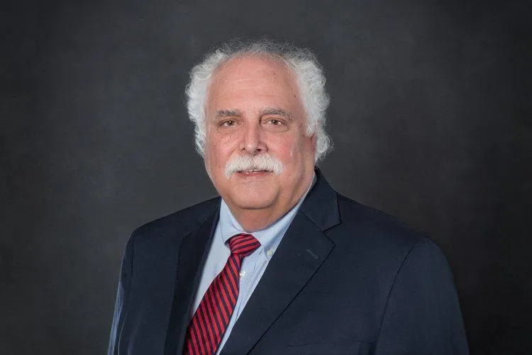 Professional headshot of Andrew J. Paterno, CEO of Centurion Insurance Services, wearing a navy suit and red striped tie against a dark background.