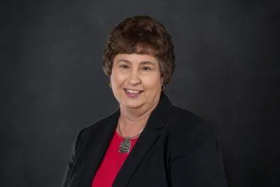 Professional headshot of Donna S. Gordon, Commercial Account Manager at Centurion Insurance Services, wearing a dark blazer and red top, posed against a dark background.