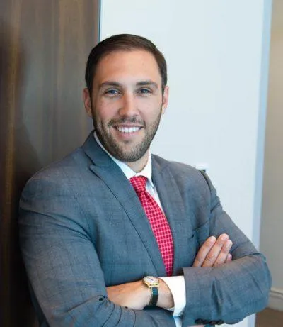 Professional headshot of Jason Wilson, Account Executive at Centurion Insurance Services, wearing a gray suit with a red tie, standing with arms crossed and smiling in a modern office setting.