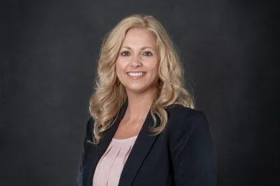 Professional headshot of Nicole L. Deems, AAI, Commercial Account Manager at Centurion Insurance Services, wearing a dark blazer and light blouse, posed against a dark background.