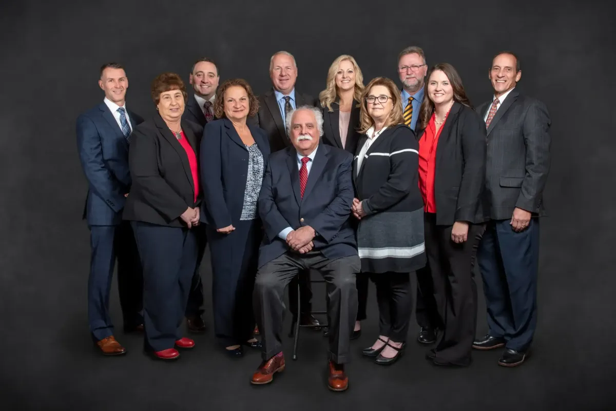 Group photo of the Centurion Insurance Services team, featuring professionally dressed staff standing and seated against a dark studio background.