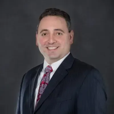 Professional portrait of Anthony J. Paterno, Senior Vice President at Centurion Insurance Services, wearing a dark pinstripe suit, white shirt, and patterned red tie against a dark background.