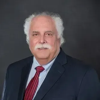 Portrait of Andrew J. Paterno, CEO of Centurion Insurance Services, wearing a navy suit, red striped tie, and light blue shirt against a dark background.