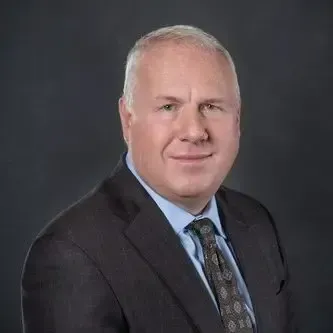 Professional portrait of Adam C. Rohrig, President of Centurion Insurance Services, wearing a dark suit, patterned tie, and light blue shirt against a dark background.