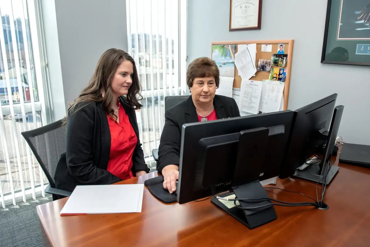 Two Centurion Insurance Services team members reviewing documents and negotiating plan renewals at a computer in a professional office setting.