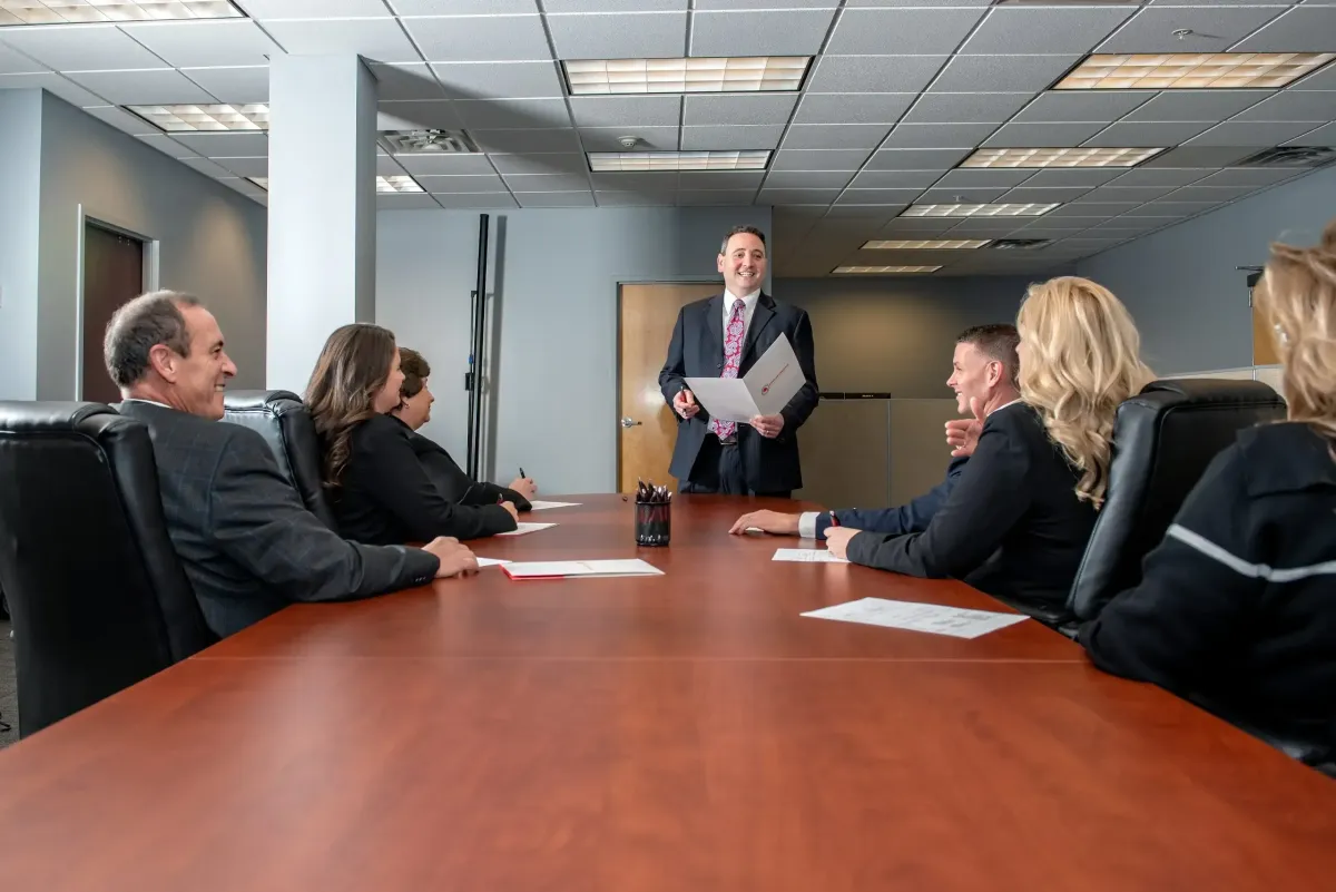 Team meeting in a corporate boardroom with a presenter standing and employees seated around a table, representing Centurion Insurance Services’ commitment to employee benefits communication and education.