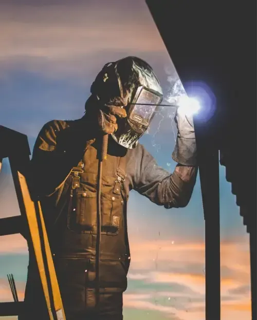 Welder in protective gear working on a metal structure at sunset, representing Centurion Insurance Services’ carrier support services and safety-focused loss control solutions.