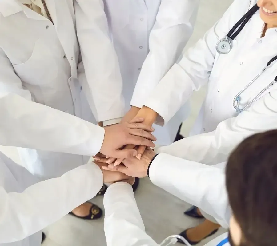 Group of healthcare professionals in white coats joining hands in a huddle, symbolizing teamwork and Centurion Insurance Services’ employee benefits solutions for medical organizations.