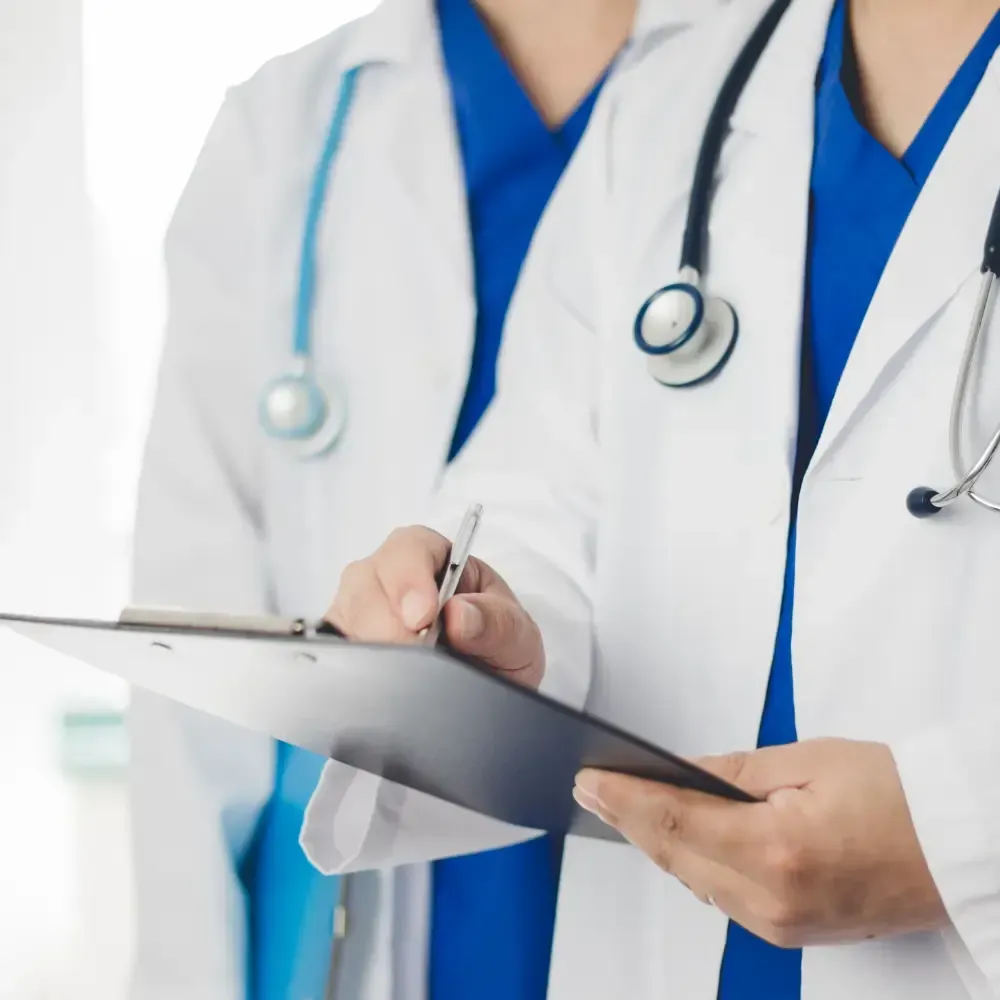 Healthcare professionals wearing white coats and stethoscopes reviewing information on a clipboard.