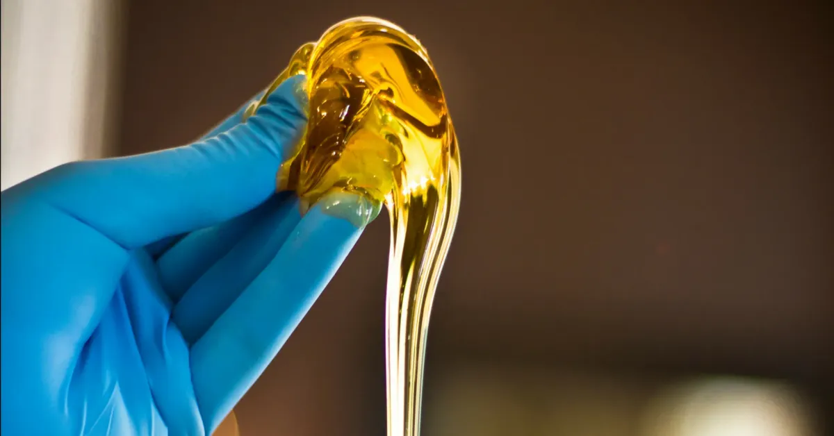 Hand wearing a blue glove holding a golden sugaring paste, illustrating skincare techniques for professionals in the sugaring industry.