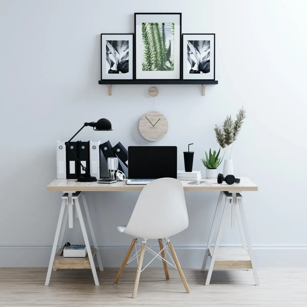 Modern home office setup with a minimalist desk, laptop, black desk lamp, and decorative plants, featuring framed botanical art on the wall and organized binders, emphasizing a clean and productive workspace.