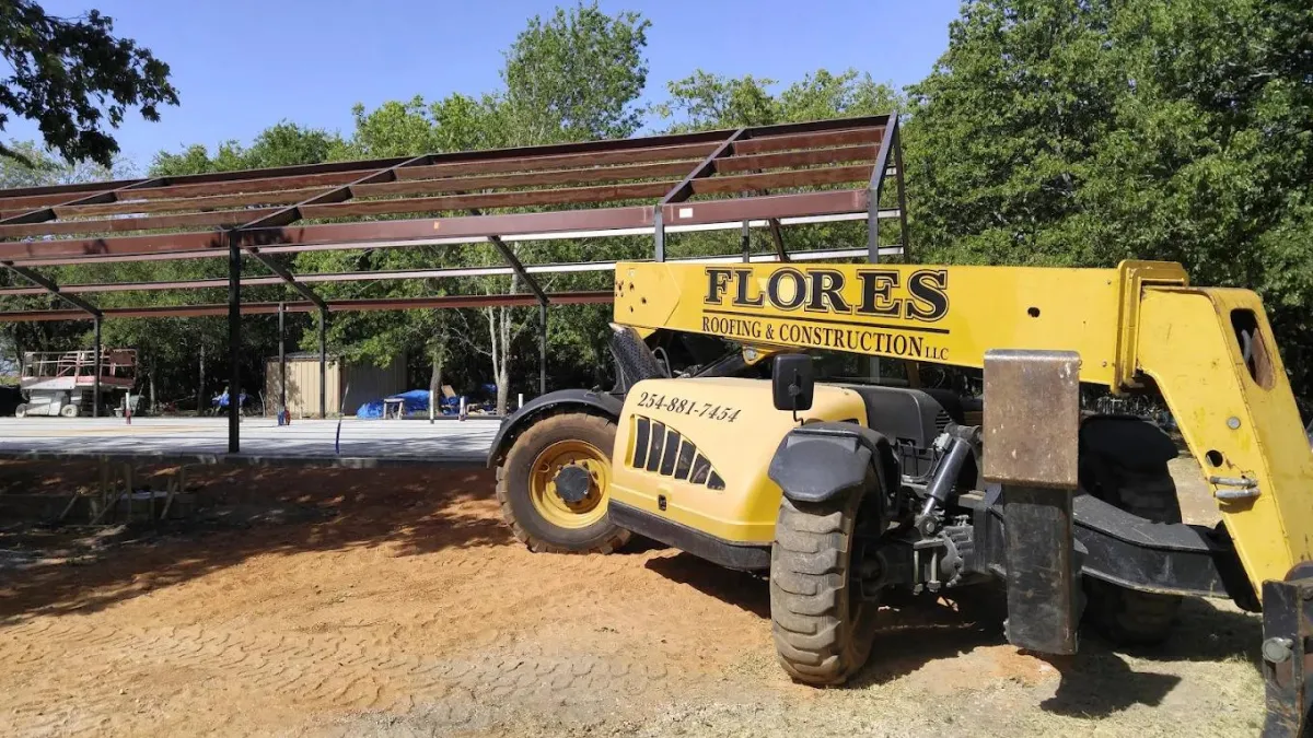Large construction lift by metal building frame with Flores Roofing & Construction logo on the side